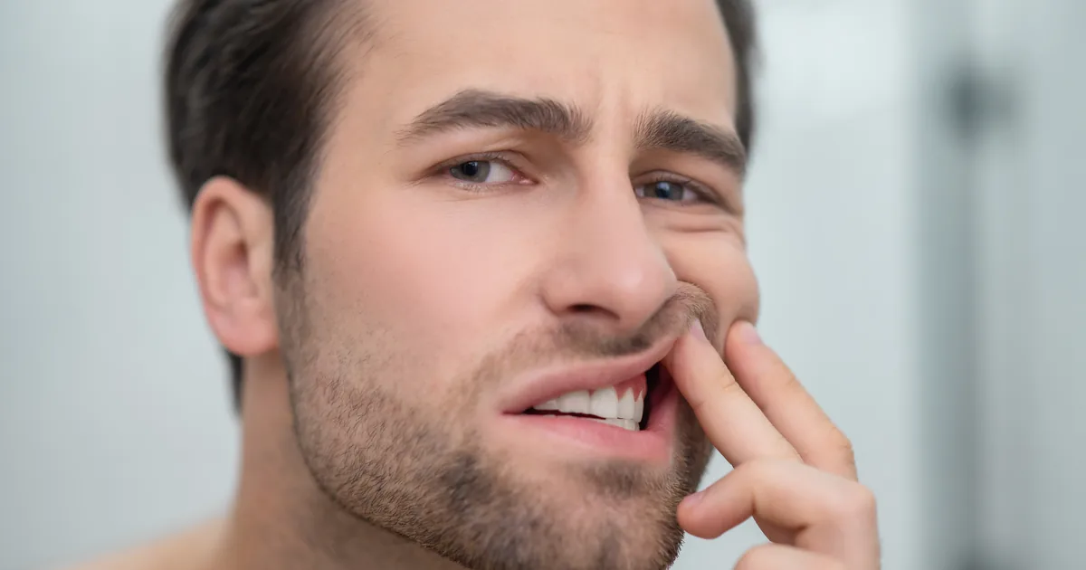 Man pulling back his lip in front of a mirror to look closely at his gums
