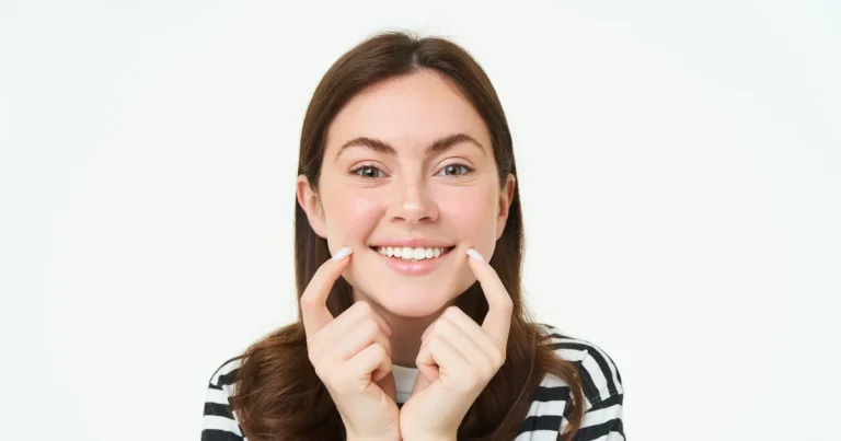 Smiling young woman framing her straight teeth with her fingers against a white background